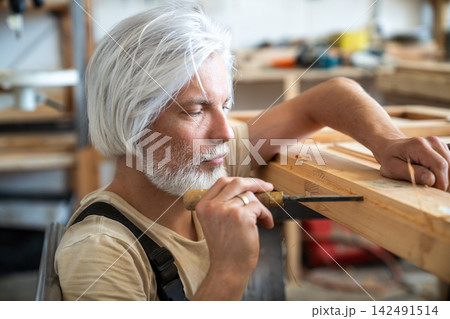 Concentrated professional craftsman restoring antique wooden furniture in carpentry workshop 142491514