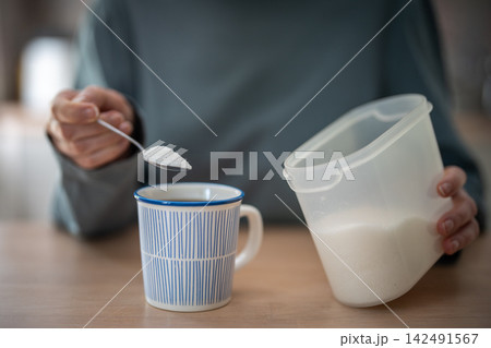 Woman holds spoonful of white sugar over coffee, showing habitual sugar dependence at home. Woman holds spoonful of white sugar over coffee, showing habitual sugar dependence at home. 142491567