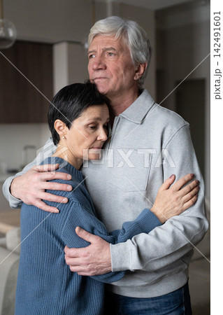 Tired mature wife with closed eyes being tightly embraced by husband, seeking emotional support Tired mature wife with closed eyes being tightly embraced by husband, seeking emotional support 142491601