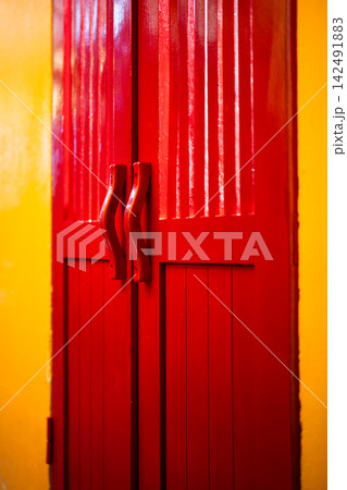 Red wooden double doors with handles on yellow wall at vintage building in Hoi An city Vietnam. Red wooden double doors with handles on yellow wall at vintage building in Hoi An city Vietnam. 142491883