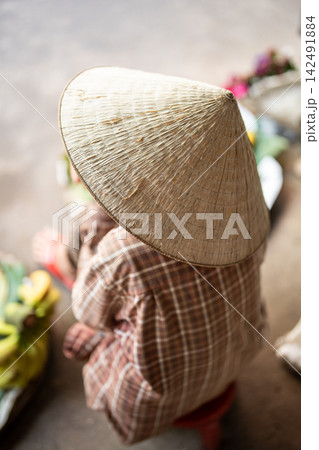 Unrecognizable street food market seller in traditional conical hat sitting waiting for customers. 142491884