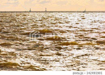 Yachtsmen are sitting amicably on board the boat, sailing boat is in sailing regatta in the Gulf of Finland at sunset, magic splashing water, teamwork Yachtsmen are sitting amicably on board the boat, sailing boat is in sailing regatta in the Gulf of Finland at sunset, magic splashing water, teamwork 142491901