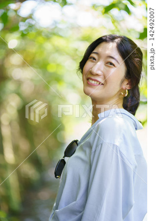 緑の玉ボケを背景に肩越しに振り返って微笑む30代の日本人女性 142492007