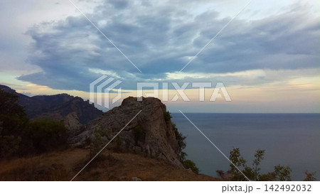 scenic rocky cliff with natural arch and panoramic view of calm sea under cloudy sunset sky scenic rocky cliff with natural arch and panoramic view of calm sea under cloudy sunset sky 142492032