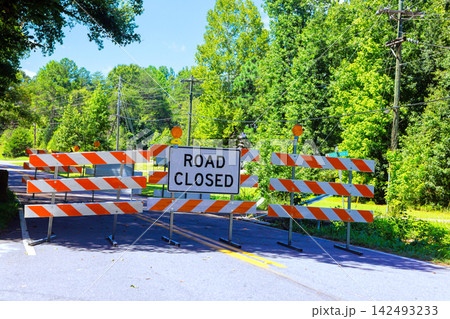 Road closed sign blocks access to rural road lined with trees 142493233
