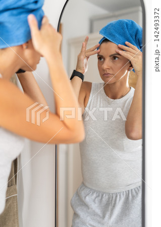 Adult woman looking into mirror in bedroom Adult woman looking into mirror in bedroom 142493372