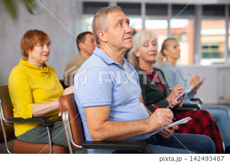 Motivated older man listening to lecture in auditorium with group Motivated older man listening to lecture in auditorium with group 142493487