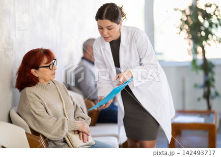 Young nurse or doctor talking with elderly woman in reception area Young nurse or doctor talking with elderly woman in reception area 142493717