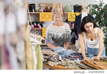 Armenian woman stands next to a mature woman near the counter in clothes store Armenian woman stands next to a mature woman near the counter in clothes store 142493950
