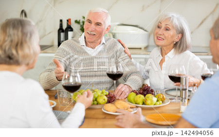Group of happy elderly people drink red wine and chat at festive table Group of happy elderly people drink red wine and chat at festive table 142494056