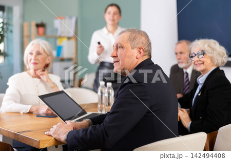 Office coworkers watching presentation while sitting at table with laptop, notes Office coworkers watching presentation while sitting at table with laptop, notes 142494408
