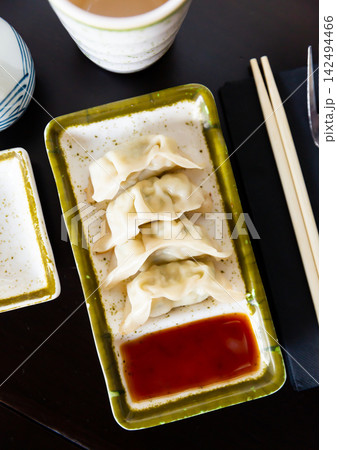 On black background stand plate with boiled gyoza dumplings served with soy sauce and chopsticks 142494466