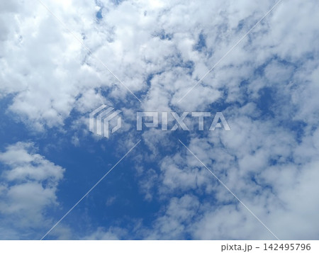 Bright blue sky filled with scattered fluffy white clouds. Natural cloudy background on a sunny summer day 142495796