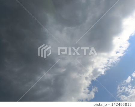 Dramatic dark grey storm clouds approaching. Contrasting weather background with a patch of blue sky Dramatic dark grey storm clouds approaching. Contrasting weather background with a patch of blue sky 142495813