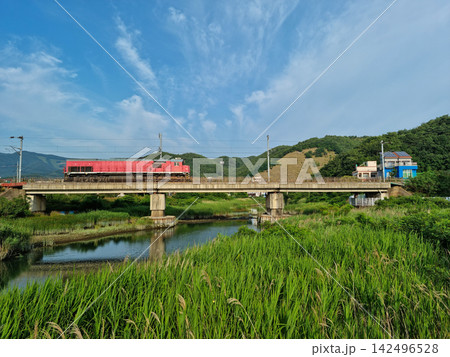 A rural scene with a red train crossing a bridge. 142496528