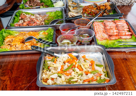 Traditional Thai food buffet with assorted dishes in metal trays. Includes stir fried vegetables, cooked shrimp, seafood salad and spicy sauces. Professional catering for Asian cuisine event. Traditional Thai food buffet with assorted dishes in metal trays. Includes stir fried vegetables, cooked shrimp, seafood salad and spicy sauces. Professional catering for Asian cuisine event. 142497211