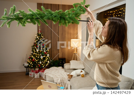 Woman decorating living room with Christmas garland Woman decorating living room with Christmas garland 142497429