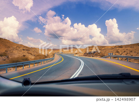 Driving a car on the mountain road in the desert. View of sandstone mountains through the windscreen. The road from Arad to the Dead Sea. Israel Driving a car on the mountain road in the desert. View of sandstone mountains through the windscreen. The road from Arad to the Dead Sea. Israel 142498907