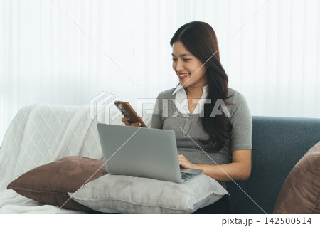 Young Asian Woman Studying Online with Laptop, Tablet, Smartphone and Headphones at Home, Adult Education and E-Learning 142500514
