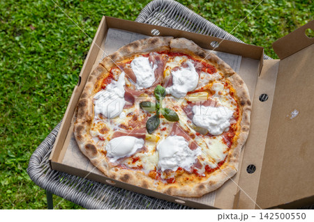 Freshly Baked Burrata and Prosciutto Pizza on Patio Chair in Garden Freshly Baked Burrata and Prosciutto Pizza on Patio Chair in Garden 142500550