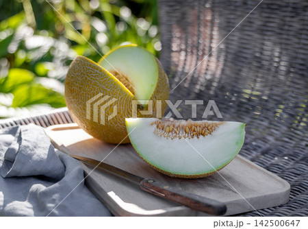 Cut Melon on Wooden Tray on Wicker Chair in Sunny Summer Garden Cut Melon on Wooden Tray on Wicker Chair in Sunny Summer Garden 142500647