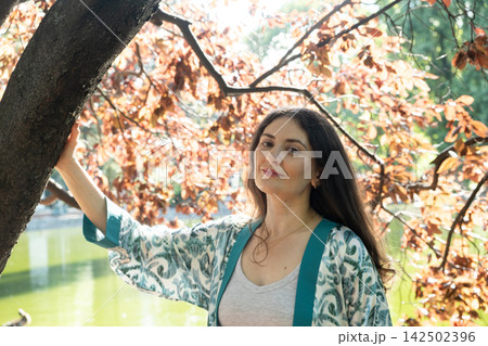 Portrait of attractive woman touching tree trunk in park near pond Portrait of attractive woman touching tree trunk in park near pond 142502396