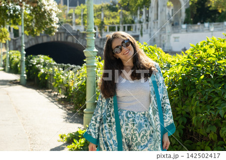 Portrait of happy brunette woman walking in sunlit park expressing femininity and confidence Portrait of happy brunette woman walking in sunlit park expressing femininity and confidence 142502417