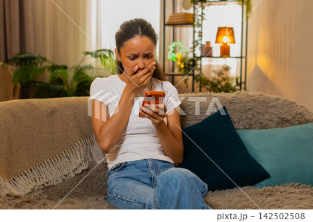 African American young woman on home sofa sighing with disappointment after bad news on smartphone 142502508