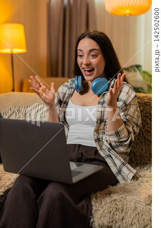 Young woman on home sofa celebrates great result on laptop raising hands with joyful victory smile Young woman on home sofa celebrates great result on laptop raising hands with joyful victory smile 142502600