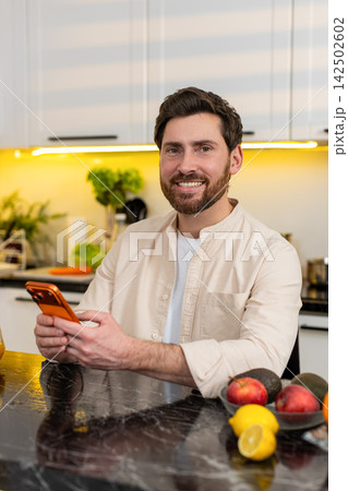 Middle-aged man happy smiling using smartphone in home kitchen browsing recipe tips and online chat 142502602