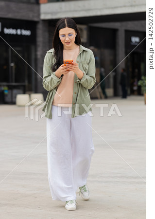 Young woman taking notes during wireless call walking in city street near office center for business 142502729
