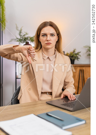 Businesswoman shows thumbs down at laptop dislike gesture unhappy face reacts to bad result review Businesswoman shows thumbs down at laptop dislike gesture unhappy face reacts to bad result review 142502730