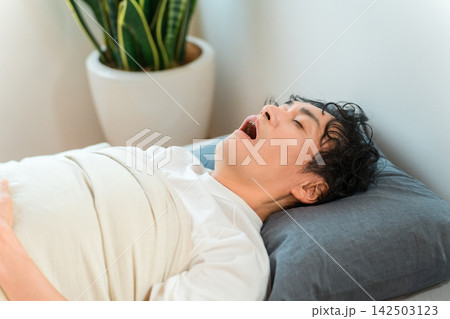 ベッドで口を開けて眠る男性、いびきや睡眠トラブルのイメージ ベッドで口を開けて眠る男性、いびきや睡眠トラブルのイメージ 142503123
