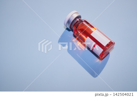 Vial containing red liquid for vaccine or treatment, casting blue shadow 142504021
