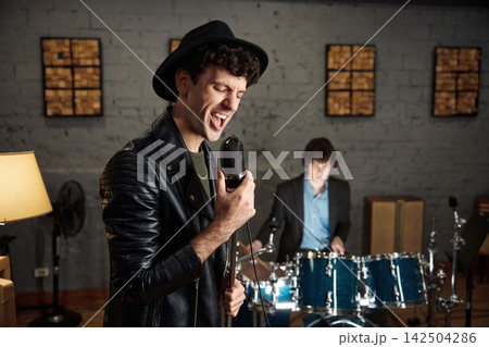 Energetic singer gripping vintage microphone in gritty rehearsal studio Energetic singer gripping vintage microphone in gritty rehearsal studio 142504286