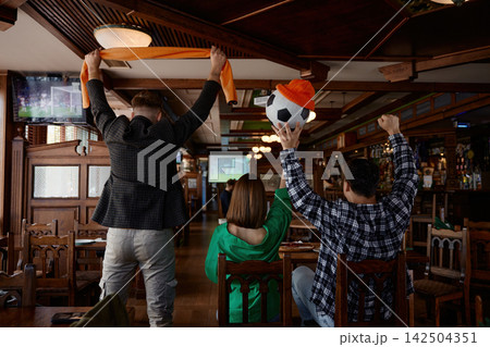 Friends cheer enthusiastically at pub. Lively pub scene with friends celebrating match 142504351