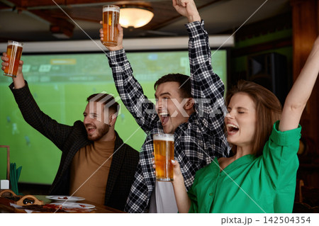 Group of friends celebrating with beer cups enthusiastically with raised arms 142504354