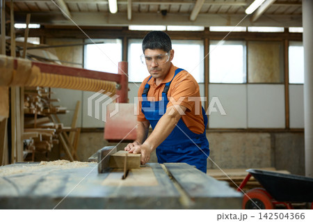 Skilled carpenter carefully feeds timber into blade with safety equipment and efficiency Skilled carpenter carefully feeds timber into blade with safety equipment and efficiency 142504366