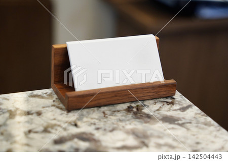 Blank white business card mockup on a wooden holder over marble desk Blank white business card mockup on a wooden holder over marble desk 142504443