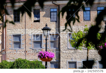 Vintage Street Lantern with Bright Purple Flowers Against Old Brick Building Creating Charming Historic European City Atmosphere Vintage Street Lantern with Bright Purple Flowers Against Old Brick Building Creating Charming Historic European City Atmosphere 142505576