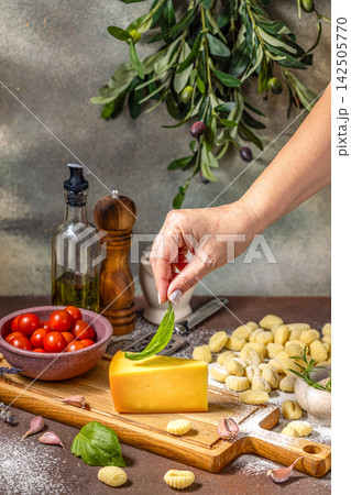 Chef placing basil leaf on cheese with gnocchi and ingredients on table 142505770