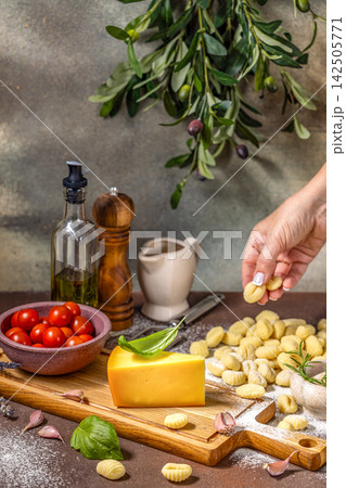 Chef placing fresh gnocchi on table with cheese, tomatoes, and olive branch 142505771