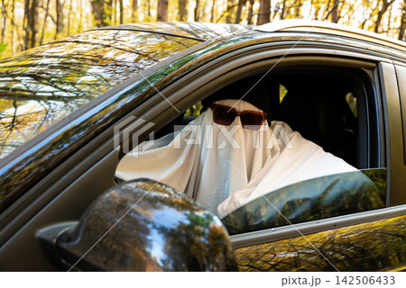 Person wearing ghost costume driving car while holding paper map, searching for direction and navigating route Person wearing ghost costume driving car while holding paper map, searching for direction and navigating route 142506433