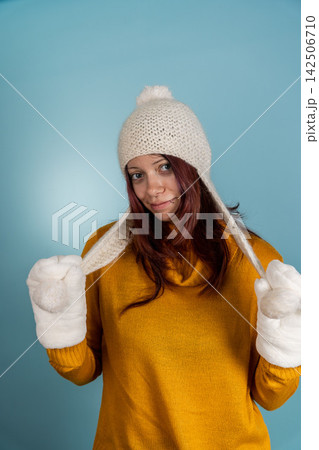 Young woman poses in winter hat and gloves against a blue background 142506710