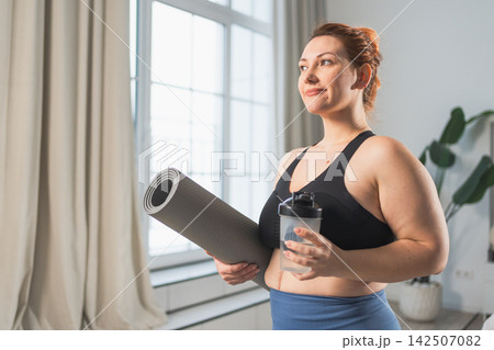 Yoga fitness sport workout training. Woman hold yoga mat bottle water ready for practicing yoga at home. Plus size female doing sports indoor. Girl in sportswear have training workout for weight loss Yoga fitness sport workout training. Woman hold yoga mat bottle water ready for practicing yoga at home. Plus size female doing sports indoor. Girl in sportswear have training workout for weight loss 142507082