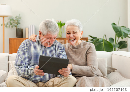 Senior old couple with tablet watching video online. Husband wife spending time together at home. Happy modern mature senior couple using tablet for family entertainment. Old people modern technology 142507168