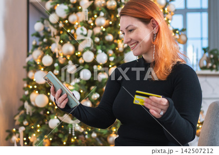 Christmas shopping. Woman shopping online holding smartphone paying with gold credit card for Christmas presents gifts. Girl buying on Internet enter credit card details. Christmas winter holidays Christmas shopping. Woman shopping online holding smartphone paying with gold credit card for Christmas presents gifts. Girl buying on Internet enter credit card details. Christmas winter holidays 142507212