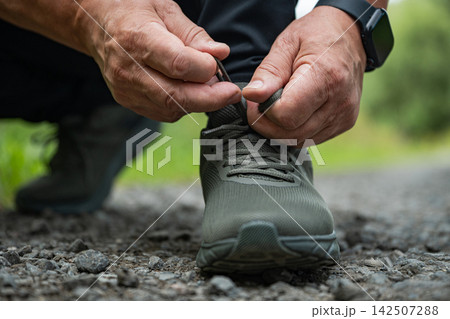 Senior man tying running shoe outdoors 142507288