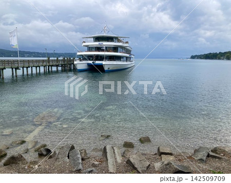 Large white passenger cruise ship docked at the wooden pier station on the calm waters of Starnberg lake in Upper Bavaria. Large white passenger cruise ship docked at the wooden pier station on the calm waters of Starnberg lake in Upper Bavaria. 142509709