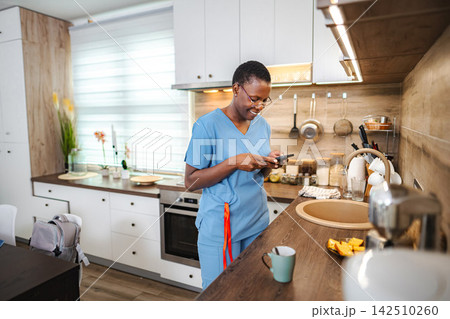 Healthcare worker texting on smartphone in kitchen at home 142510260
